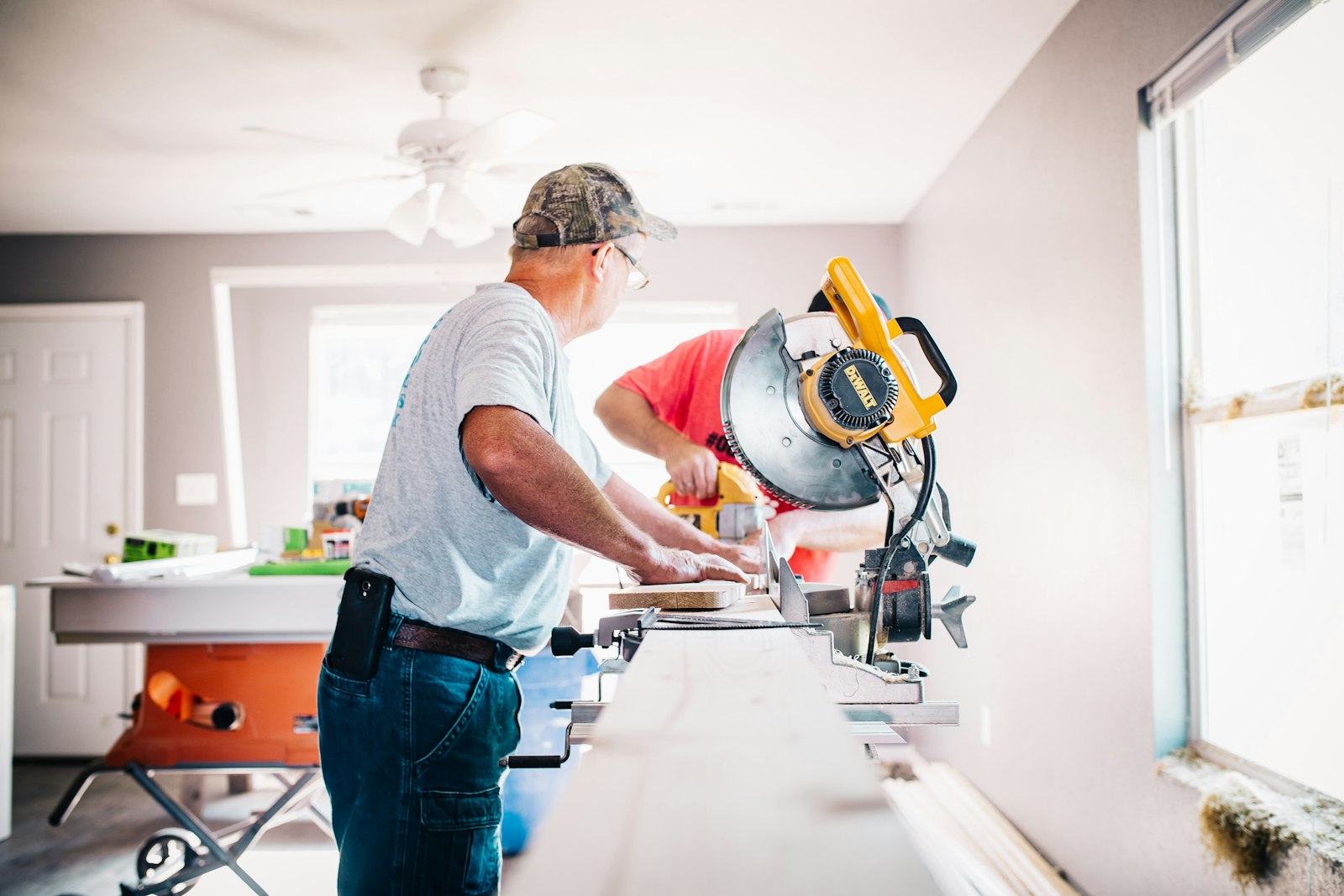 Two remodeling contractors cutting trim with a miter saw inside a home renovation