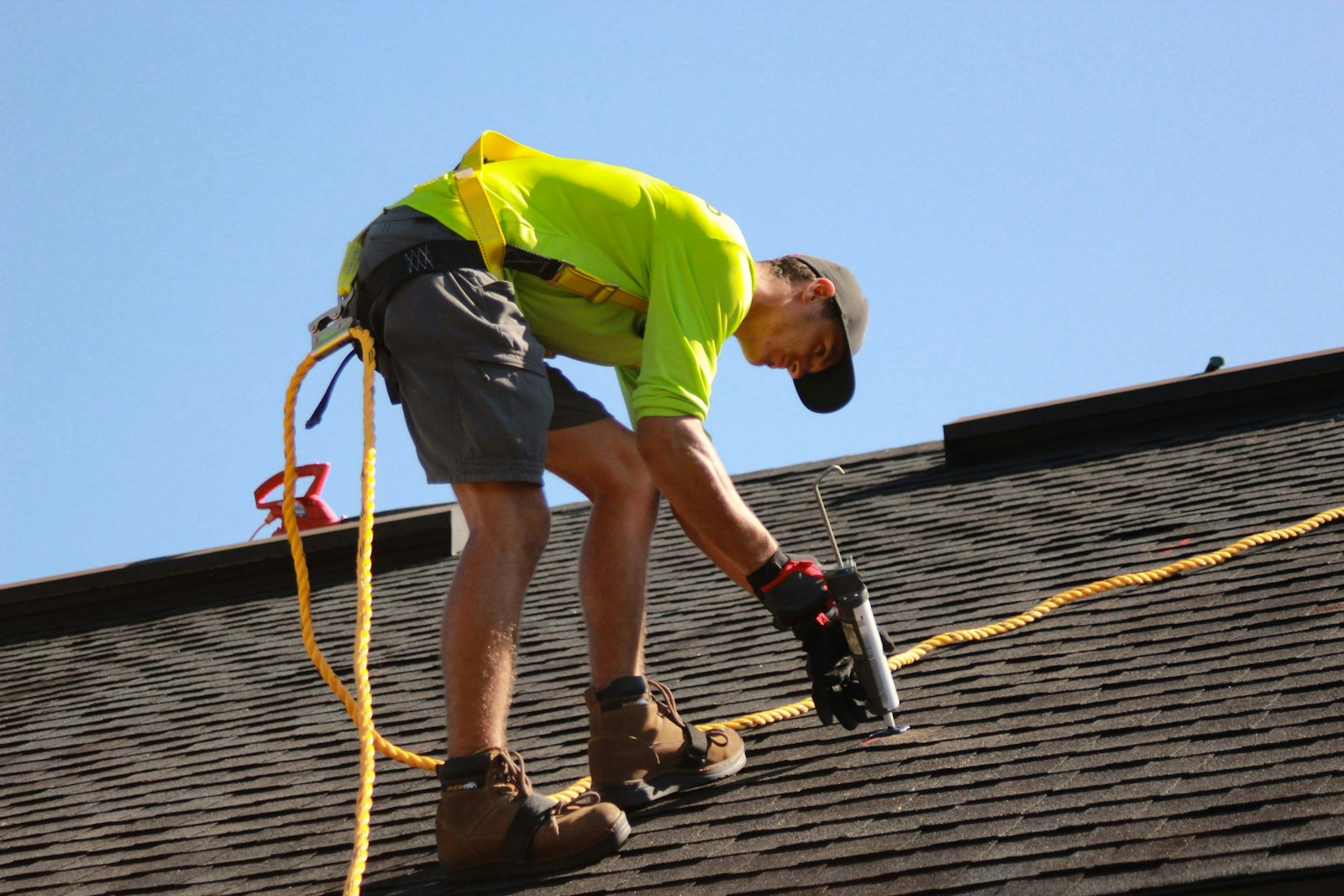 Roofer in safety harness sealing shingles on a residential roof