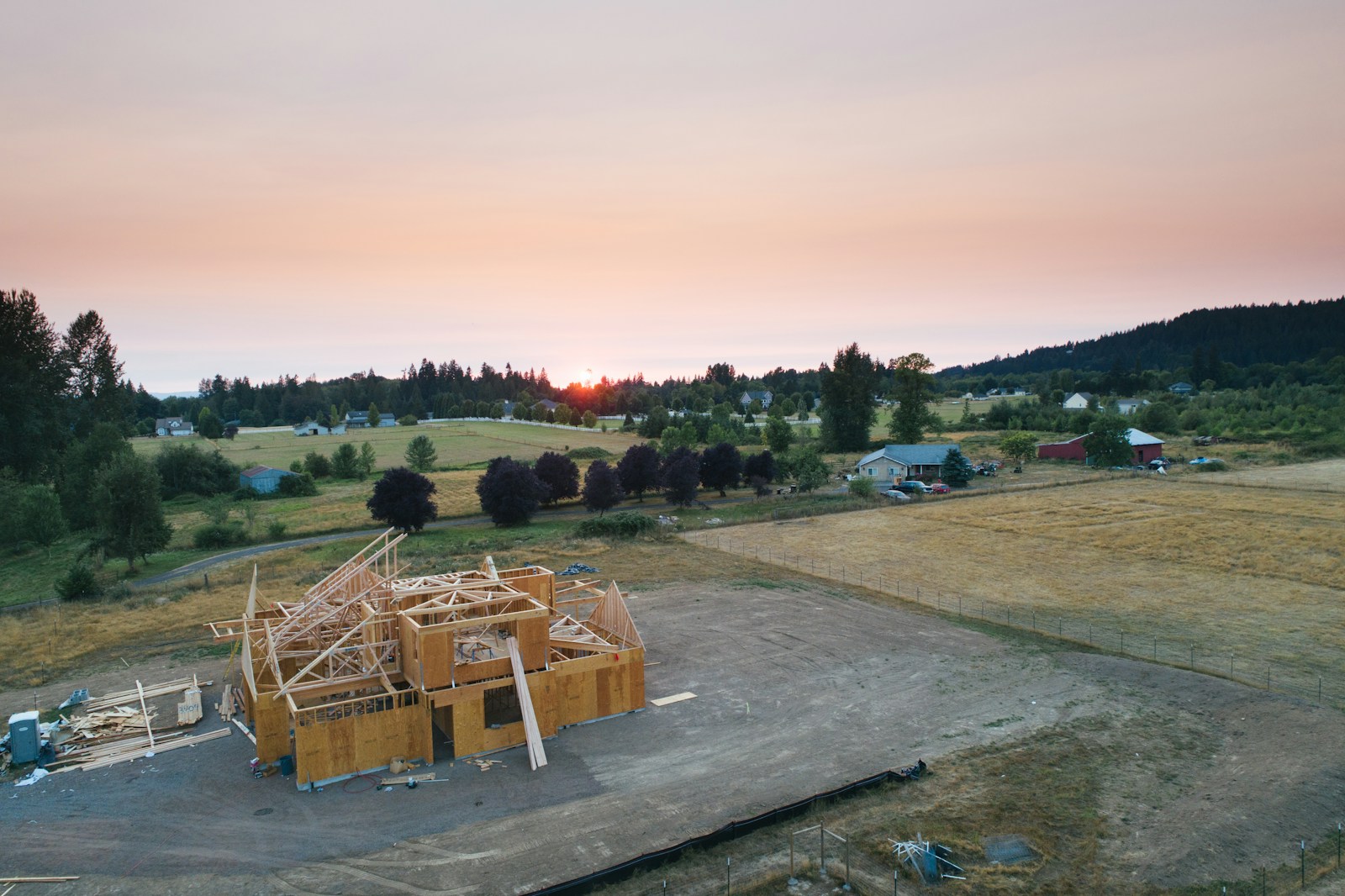 Aerial view of a custom home under construction with wood framing at sunset, surrounded by open fields