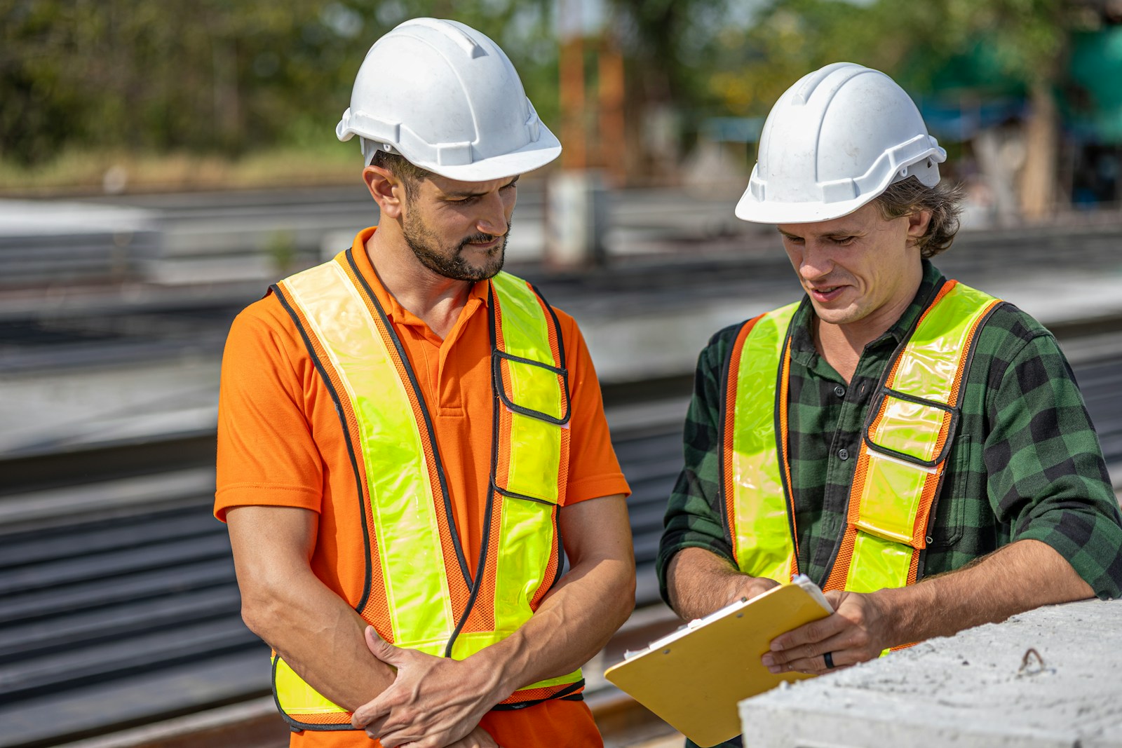 Two home-service contractors in hard hats and hi-vis vests reviewing job numbers on a clipboard at a jobsite