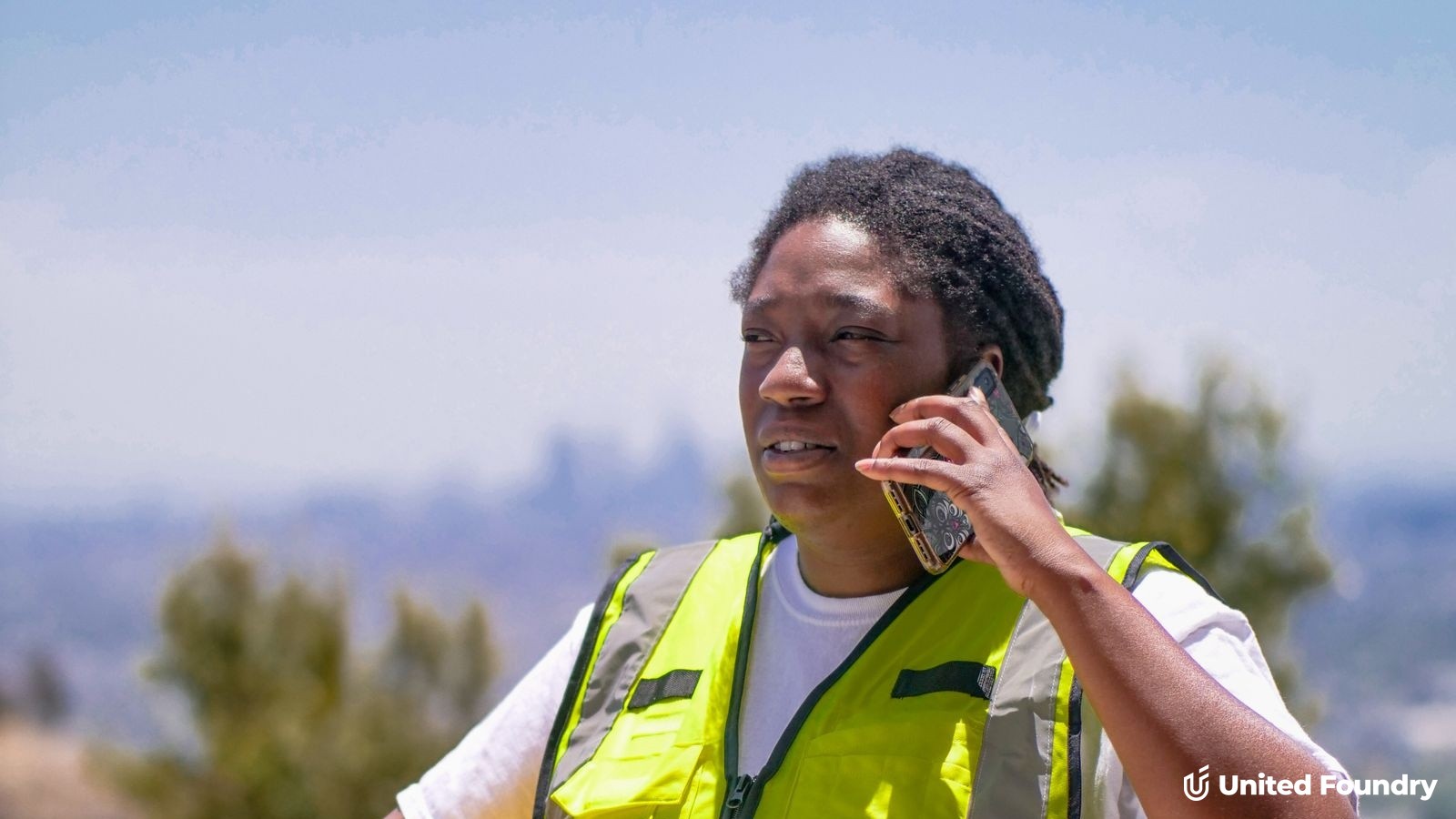 Contractor in a hi-vis safety vest taking a phone call outdoors at a job site