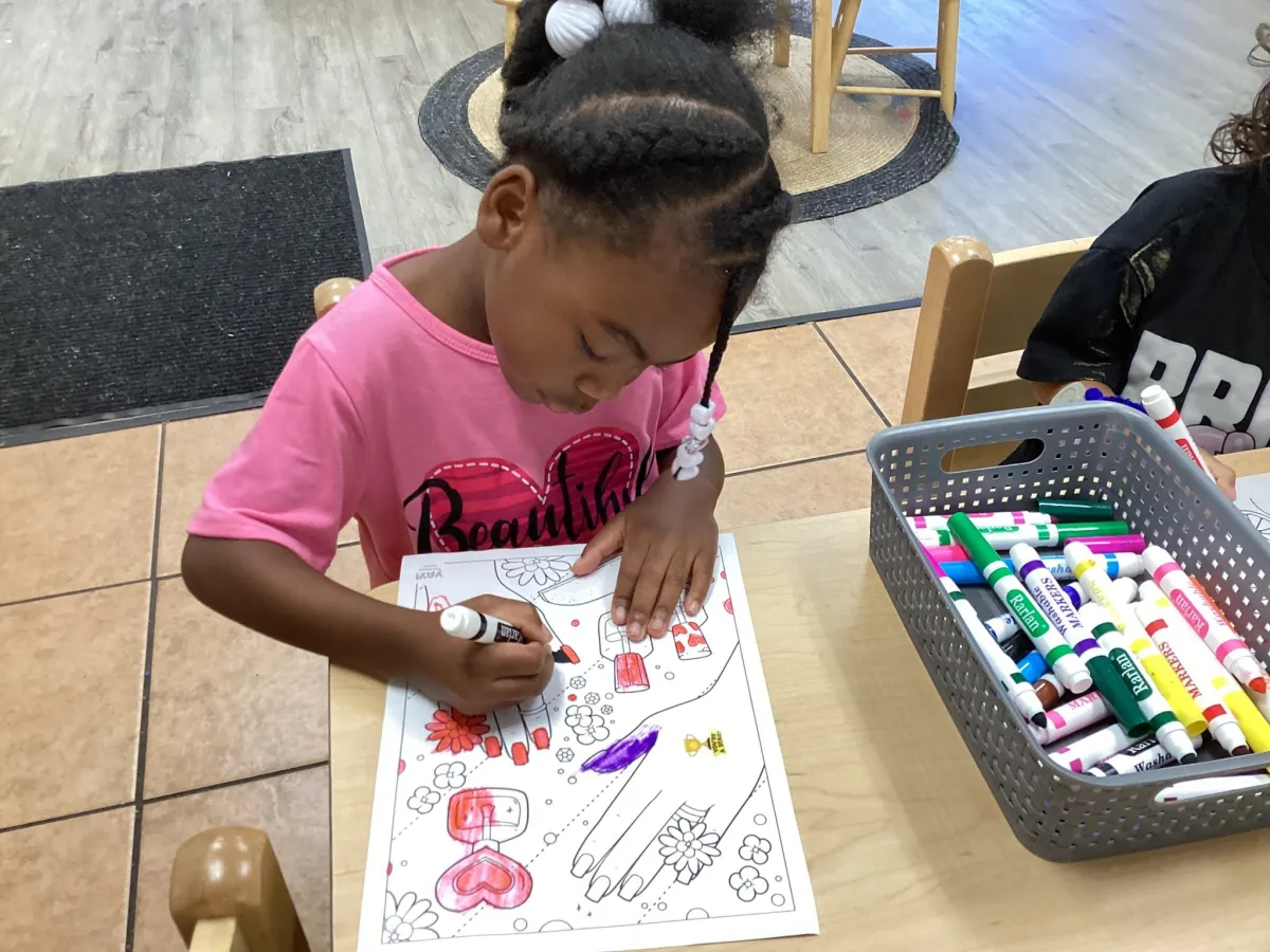 Child coloring an activity sheet at a classroom table