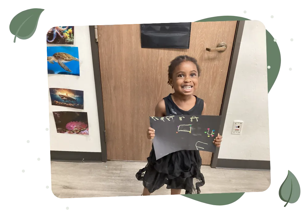 Smiling child proudly holding her artwork at BAES Education Center