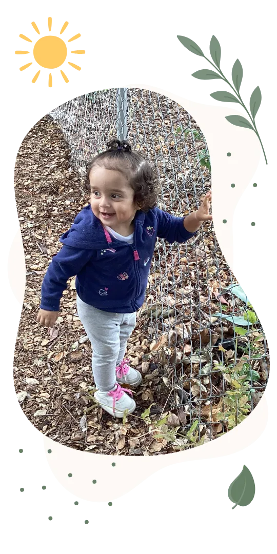 Young child exploring outdoors along a nature fence at a childcare center
