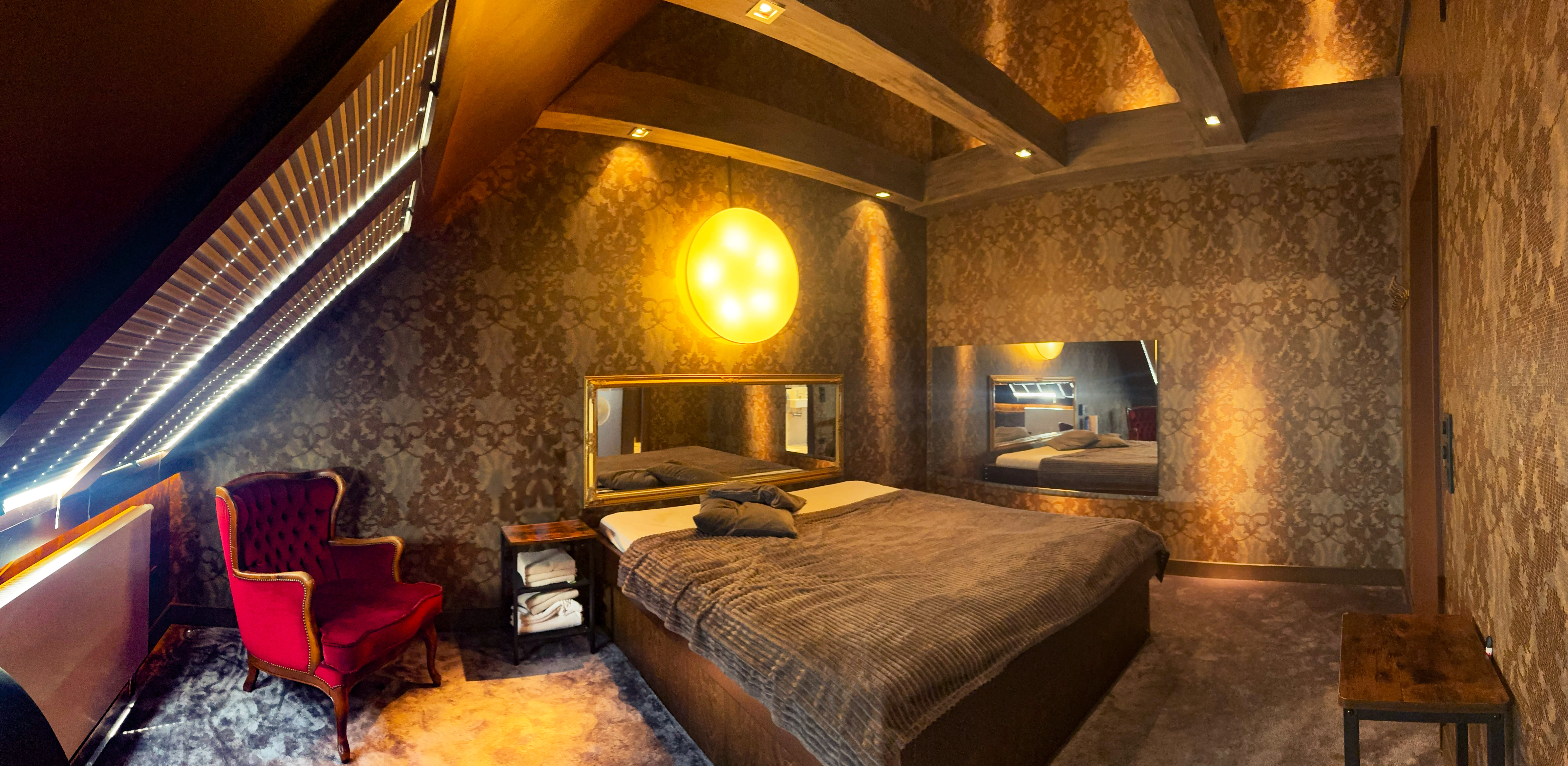 Stilvolles Zimmer der Villa Amore Düsseldorf mit Doppelbett, Spiegeln und rotem Sessel