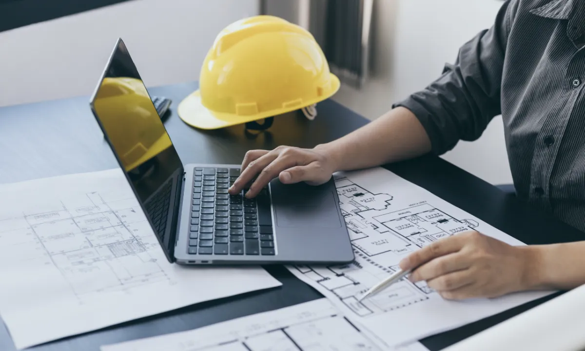 construction manager working on laptop with plans and hardhat