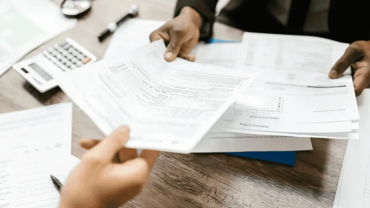 Close-up of two hands exchanging legal or corporate claim documents over a desk, symbolizing legal preparation and airtight documentation management