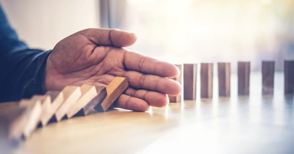 Hand stopping falling dominoes, representing how emotional awareness can interrupt unconscious leadership reactions before they affect behavior.