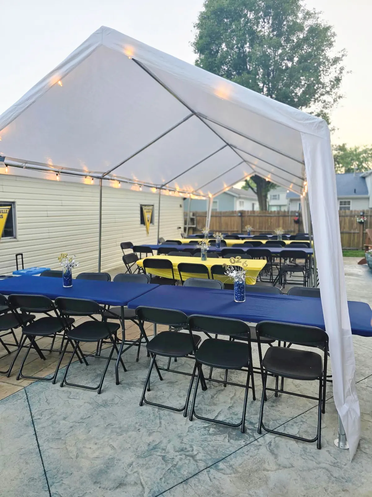 White party rental tent with, covered rectangular tables, and black folding chairs set up for a grad party