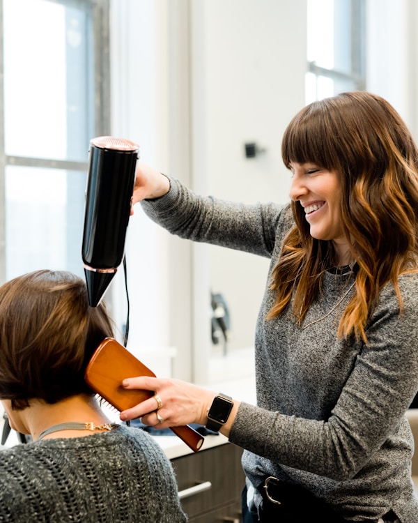 Cosmetology student blow-drying client hair during hands-on training at Rivertown School of Beauty