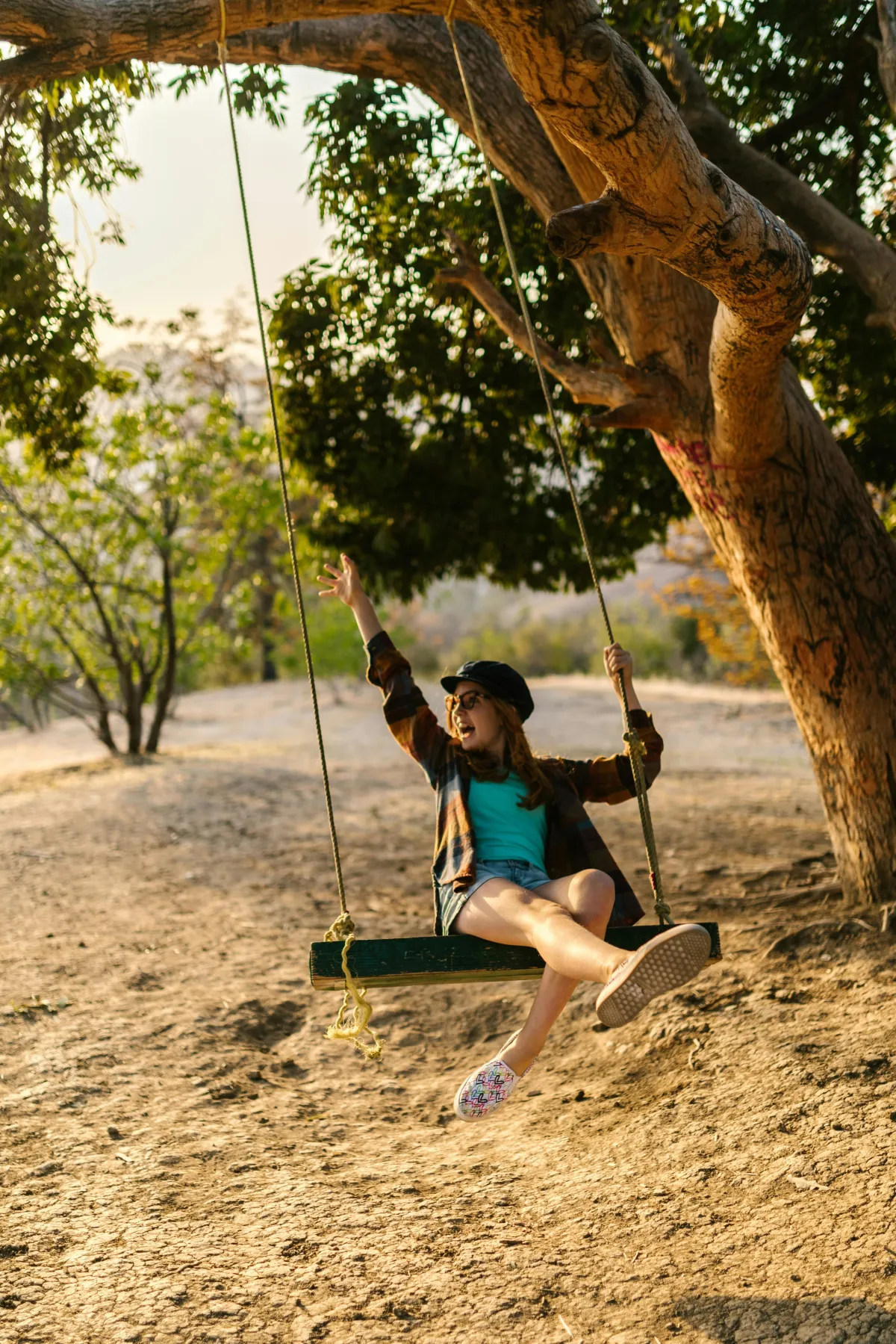 Girl swinging from a tree, laughing and enjoying the outdoors at sunset.