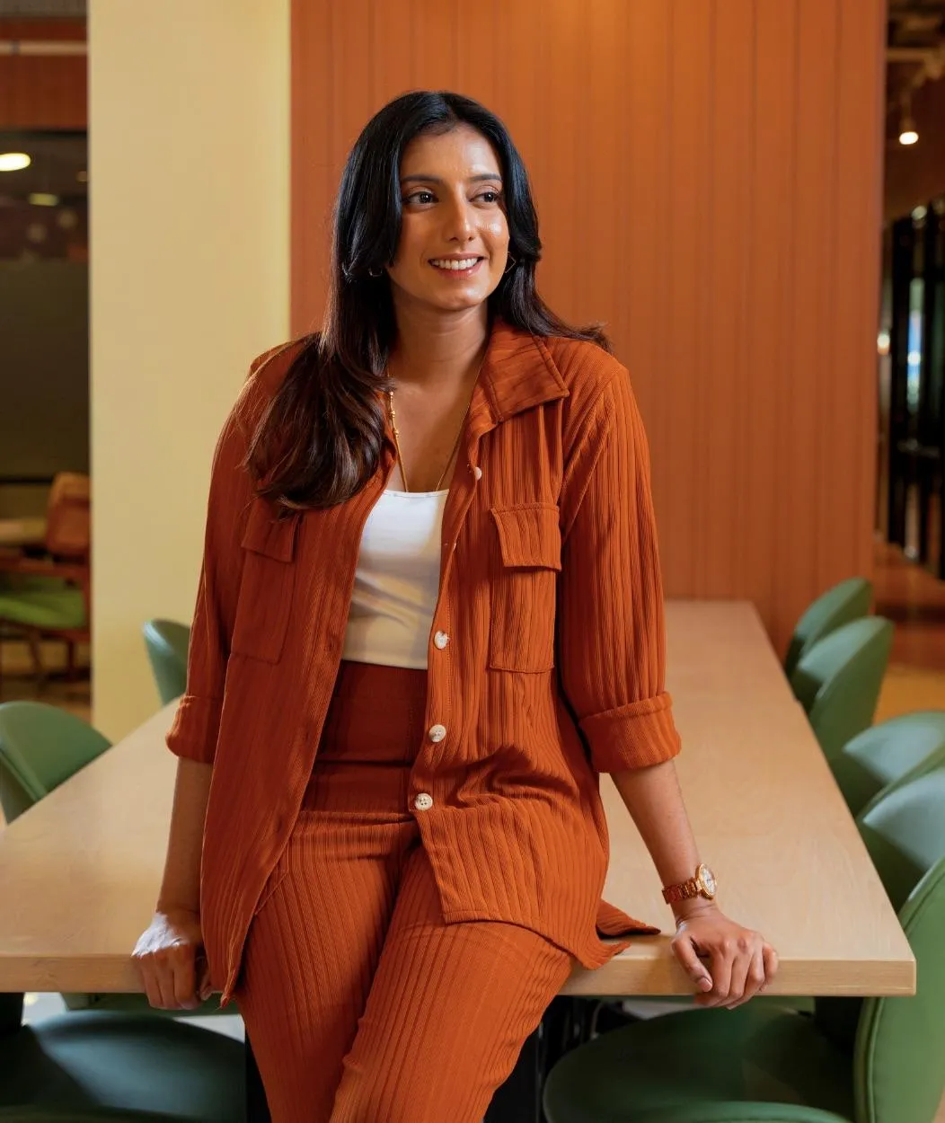 Smiling woman in business-casual attire sitting at a desk, representing workplace wellness and balance.