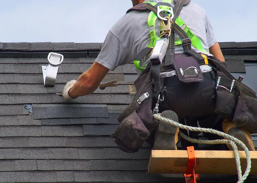 Roofer securely fastened with safety harness while performing roof repairs, emphasizing safety first.