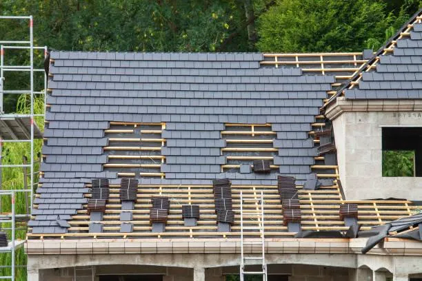 Professional roofer installing durable slate tiles on a residential roof.