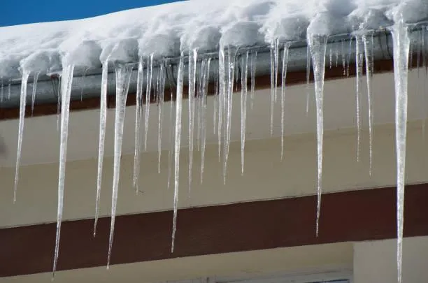 Close-up of icicles hanging from a snow-covered roof, indicating potential hazards that require professional removal services