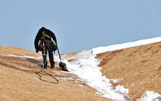 Worker removing snow from a sloped roof, demonstrating Home Star Roofing's snow removal services.