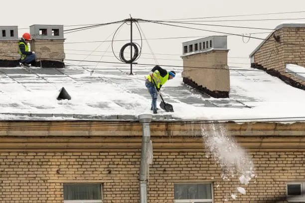 Home Star Roofing's team in action, safely clearing heavy snow off a flat roof to prevent winter damage.
