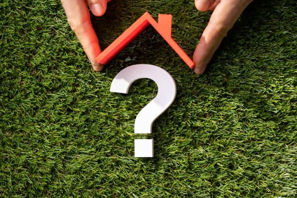 Conceptual image of a hand forming a house shape over grass with a question mark, representing the decision-making process in roof consulting.