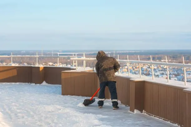 Worker shoveling snow off a flat roof to prevent structural damage, as part of Home Star Roofing's snow removal services.