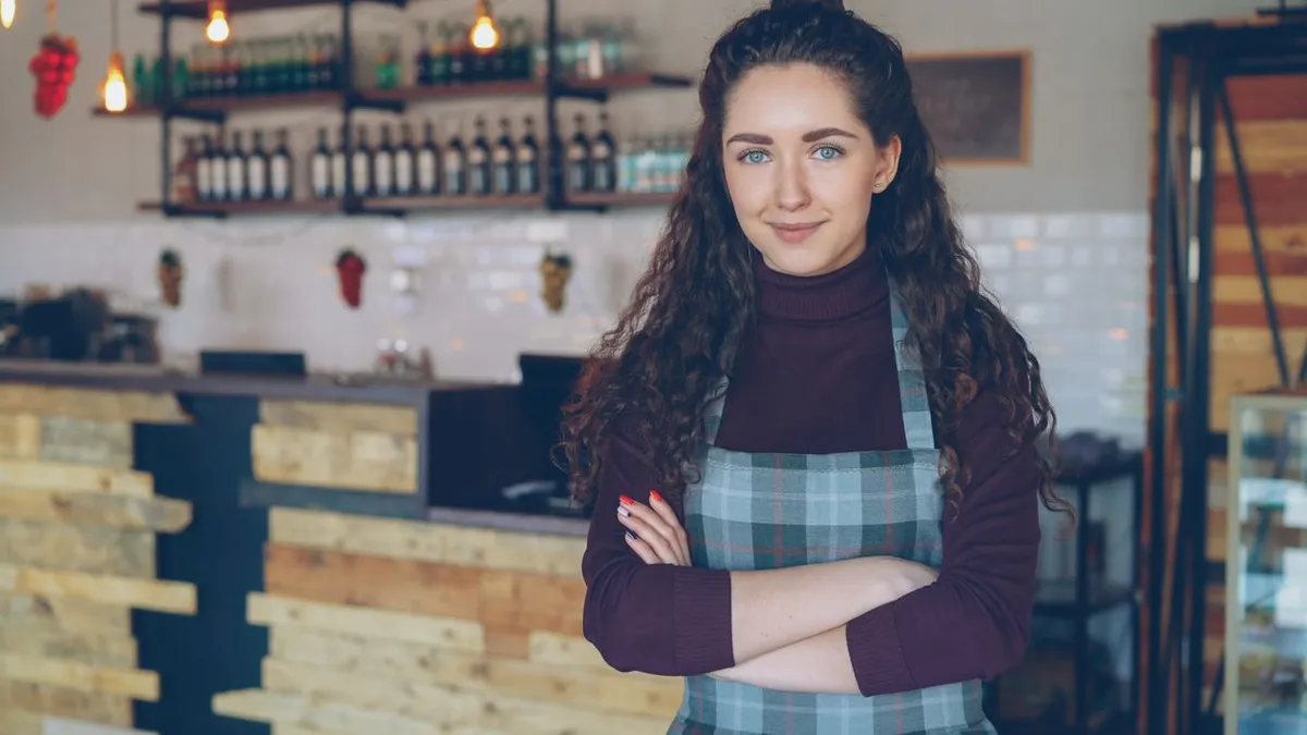 Small business owner standing with arms crossed inside a cozy local coffee shop