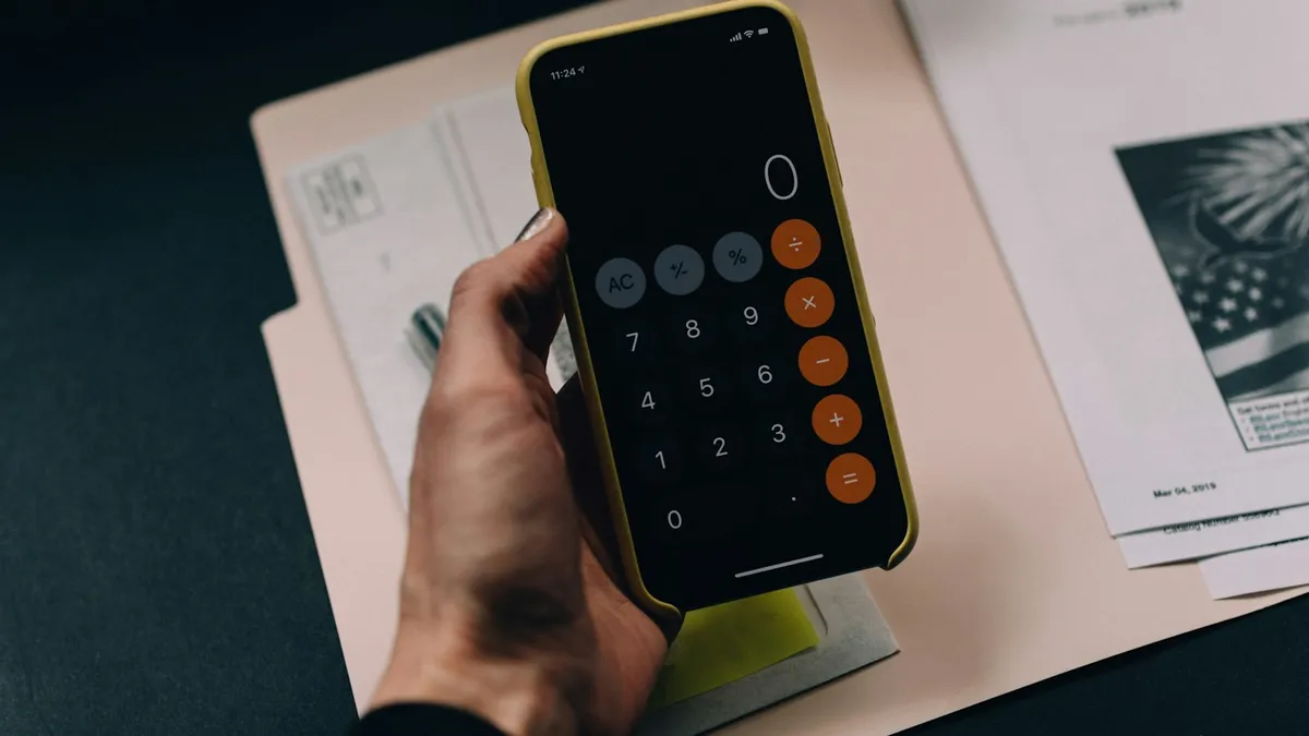 Hand holding a phone with the calculator open over paperwork