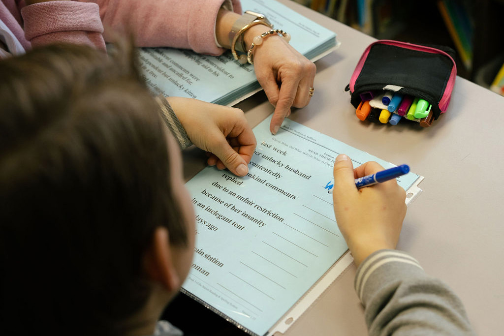 A young girl with ponytails stares curiously from behind a book.