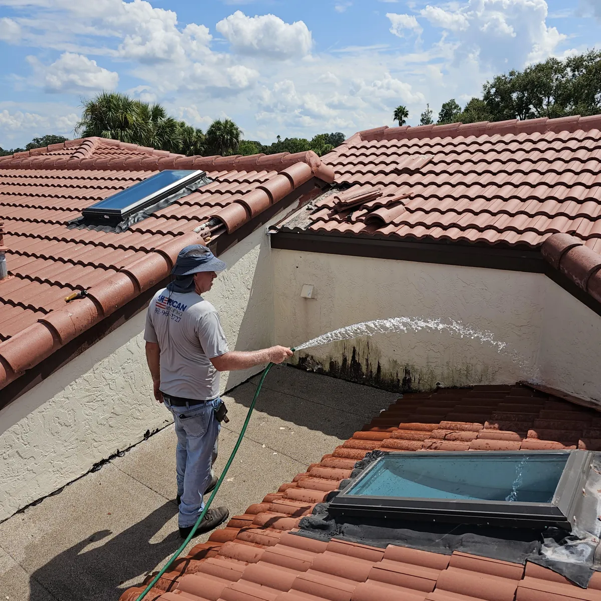 Technician water-testing wall-to-roof junction near a skylight on a tile roof to locate leaks.