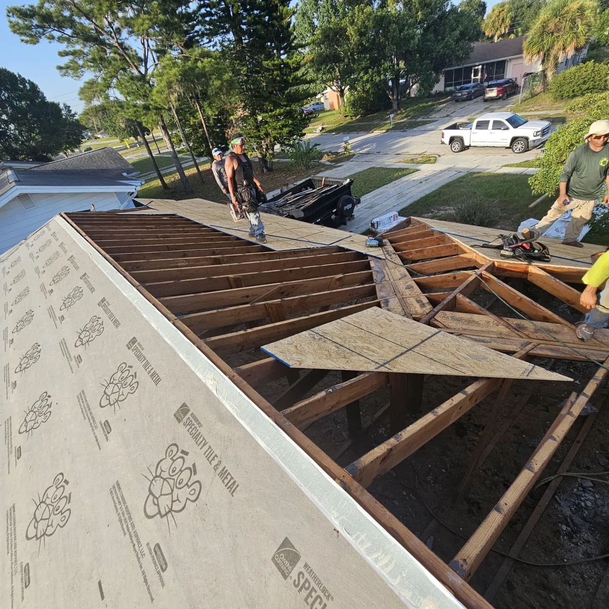 Roof tear-off exposing decking and rafters; crew installing new sheathing and underlayment.