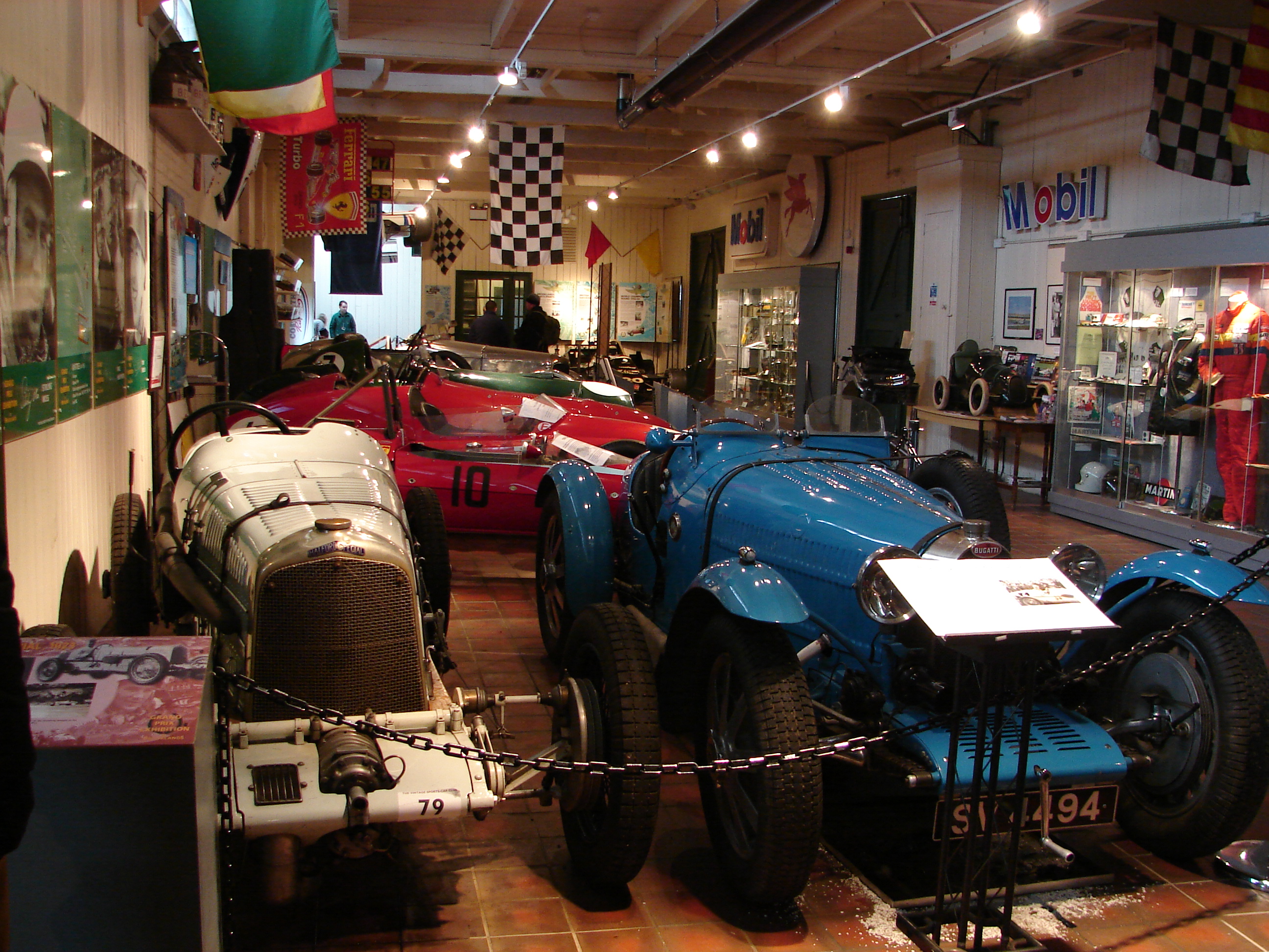 Inside a car museum with a red tiled floor and a collection of antique cars and memorabilia.
