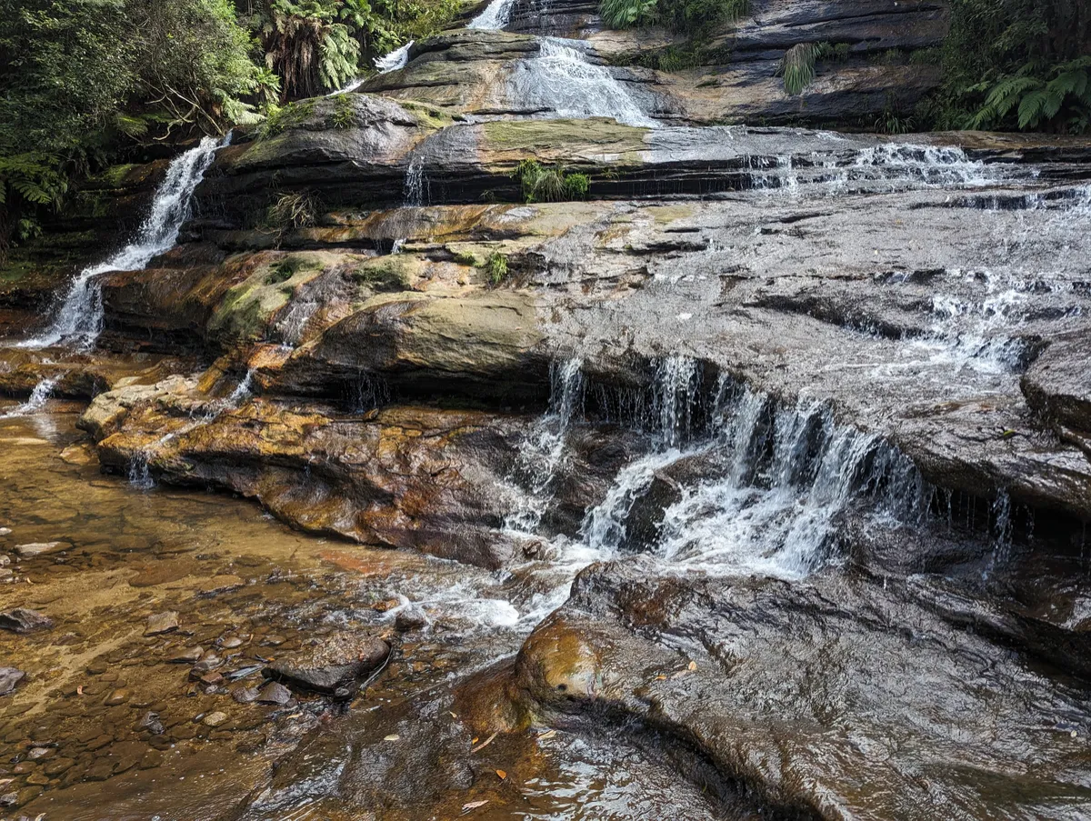 A wide Australian stream with water flowing across rocks and crevices at different speeds.