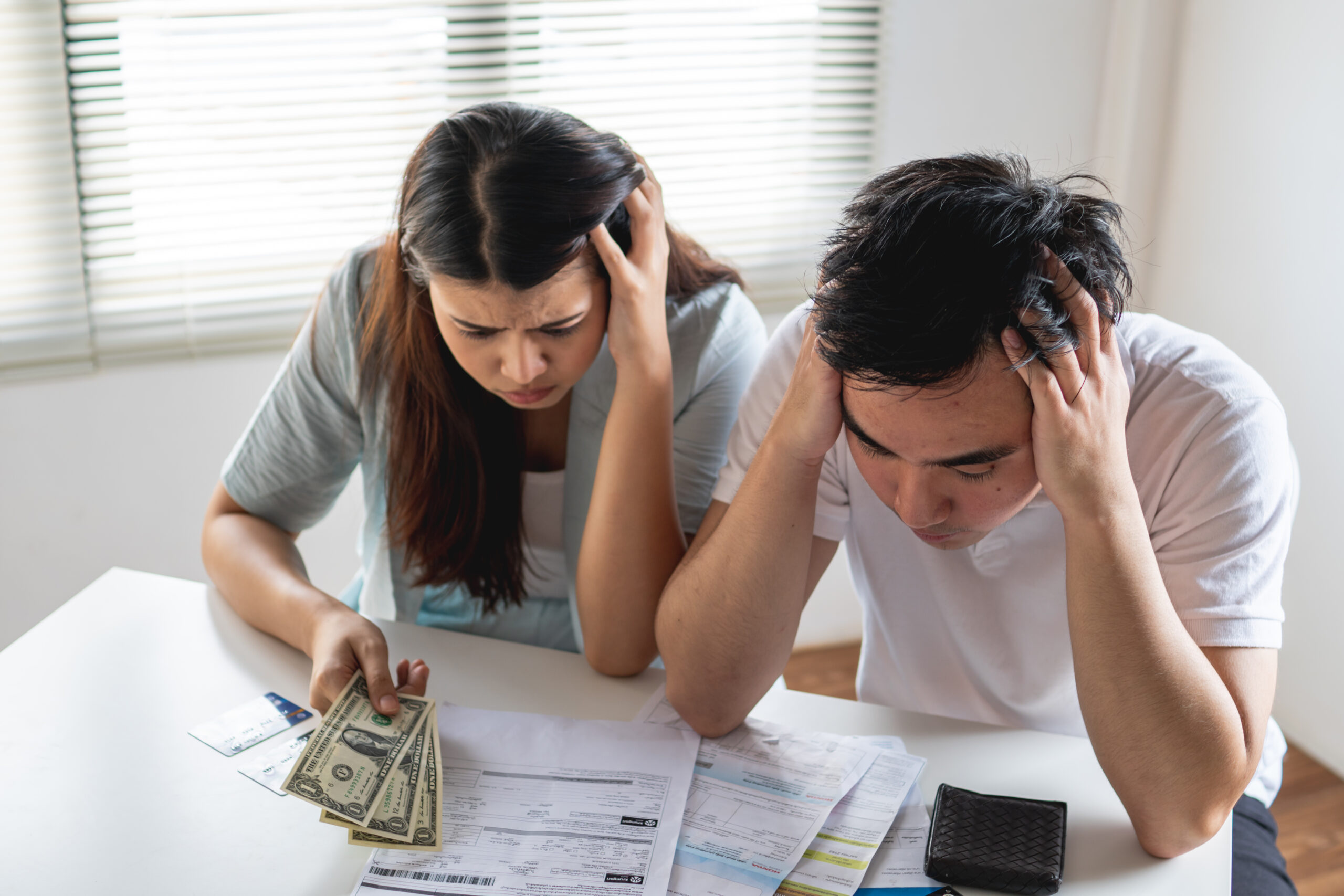 Couple stressed over financial documents and cash, representing the challenges of debt and bankruptcy.