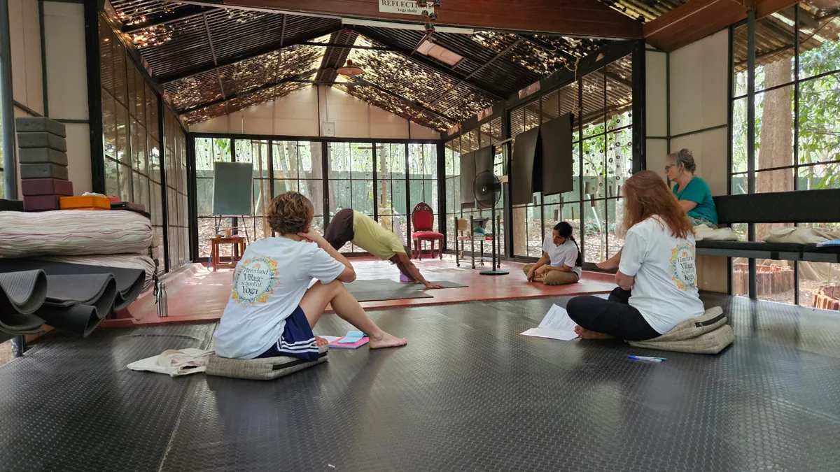 Silhouettes of people in a yoga pose outdoors facing a bright background.