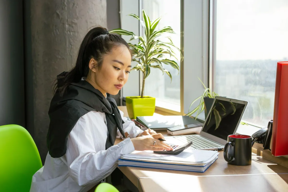 Small business owner planning IT budget on laptop with paperwork in bright office