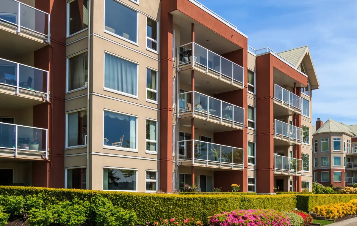 Modern low-rise apartment building with glass balconies and landscaped greenery, perfect for renters looking for spacious urban living.