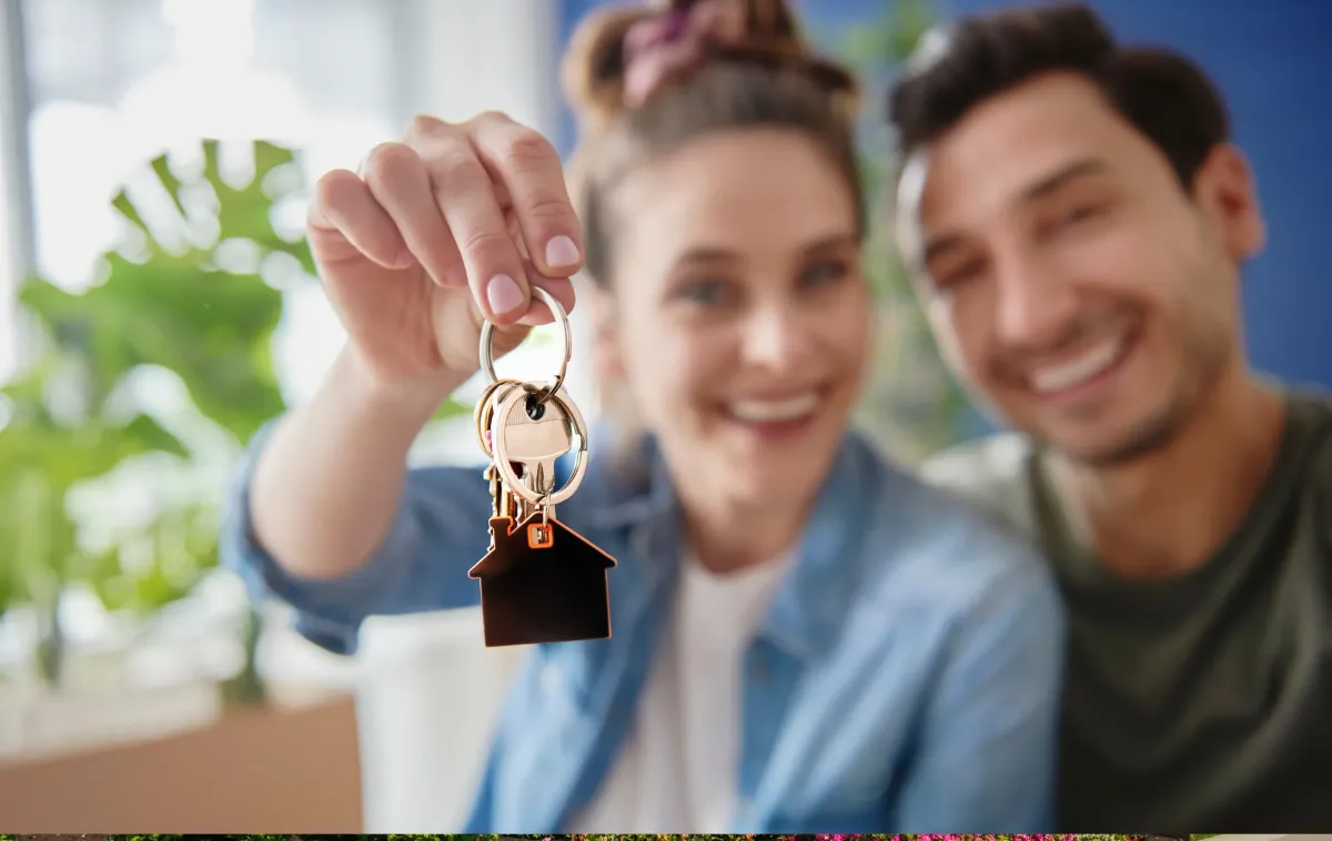 Happy couple holding house keys with a house-shaped keychain, celebrating their successful move into a new home.