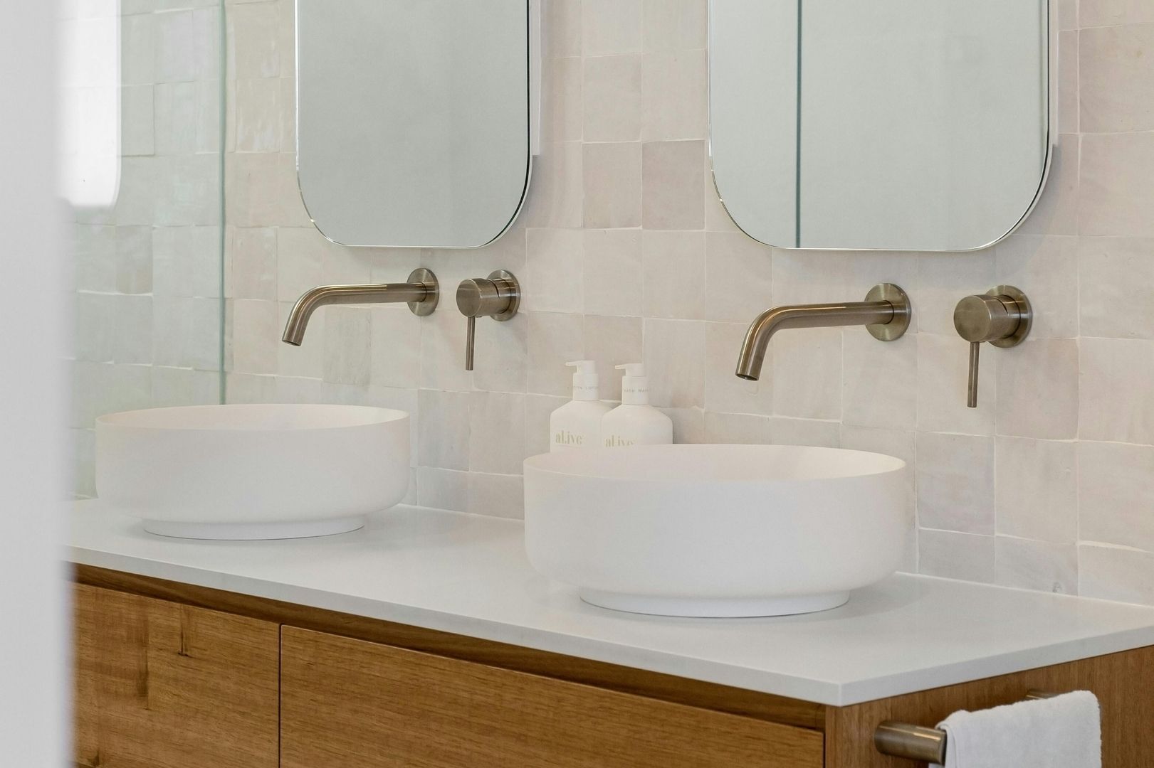 Double vasque moderne posée sur un meuble en bois clair avec robinetterie encastrée en laiton brossé.