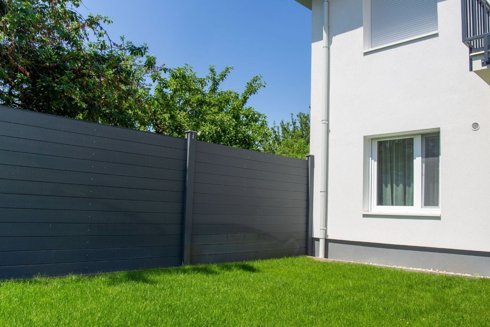 Installation d'une clôture de jardin moderne en panneaux occultants gris anthracite sur un terrain gazonné.