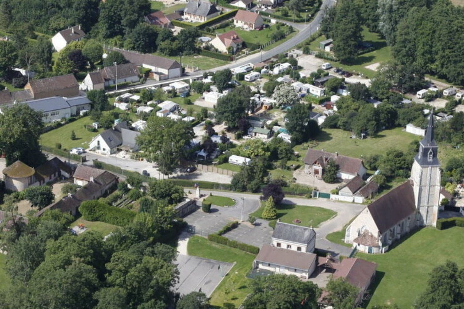 Vue aérienne de Vert-en-Drouais montrant l'église, le camping et les habitations nichées dans la verdure.