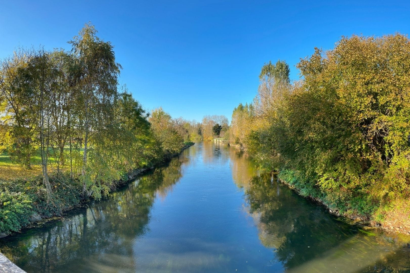 Rivière paisible traversant un cadre verdoyant et arboré à Montreuil (28), sous un ciel bleu ensoleillé.
