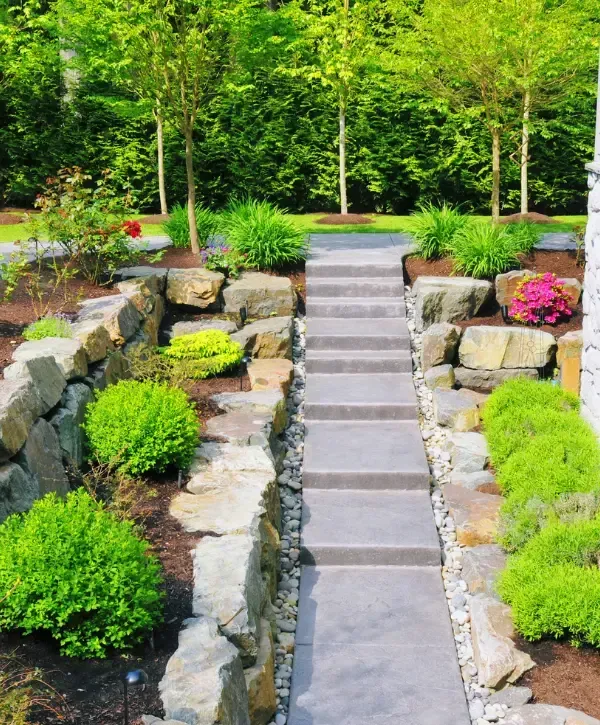 Landscaping with natural stone retaining walls, garden plants, and concrete steps leading through a landscaped yard