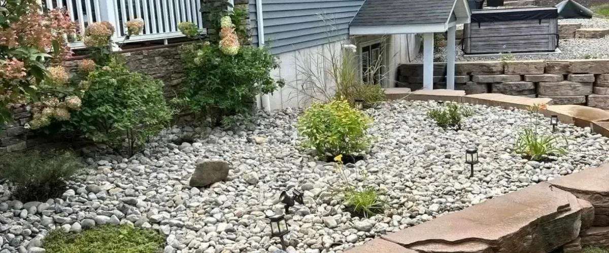 Front yard landsAVcaping with decorative river rock, stone edging, flowering plants, and natural stone steps near a home