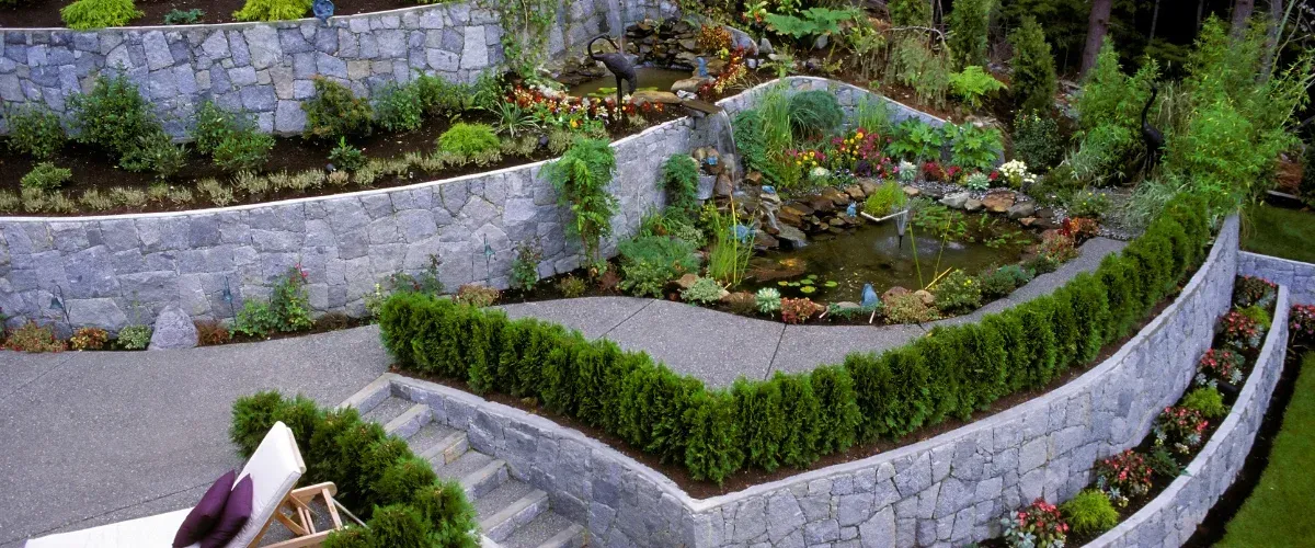 An aerial view of a terraced garden with stone retaining walls, curved pathways, and a flowing water feature.