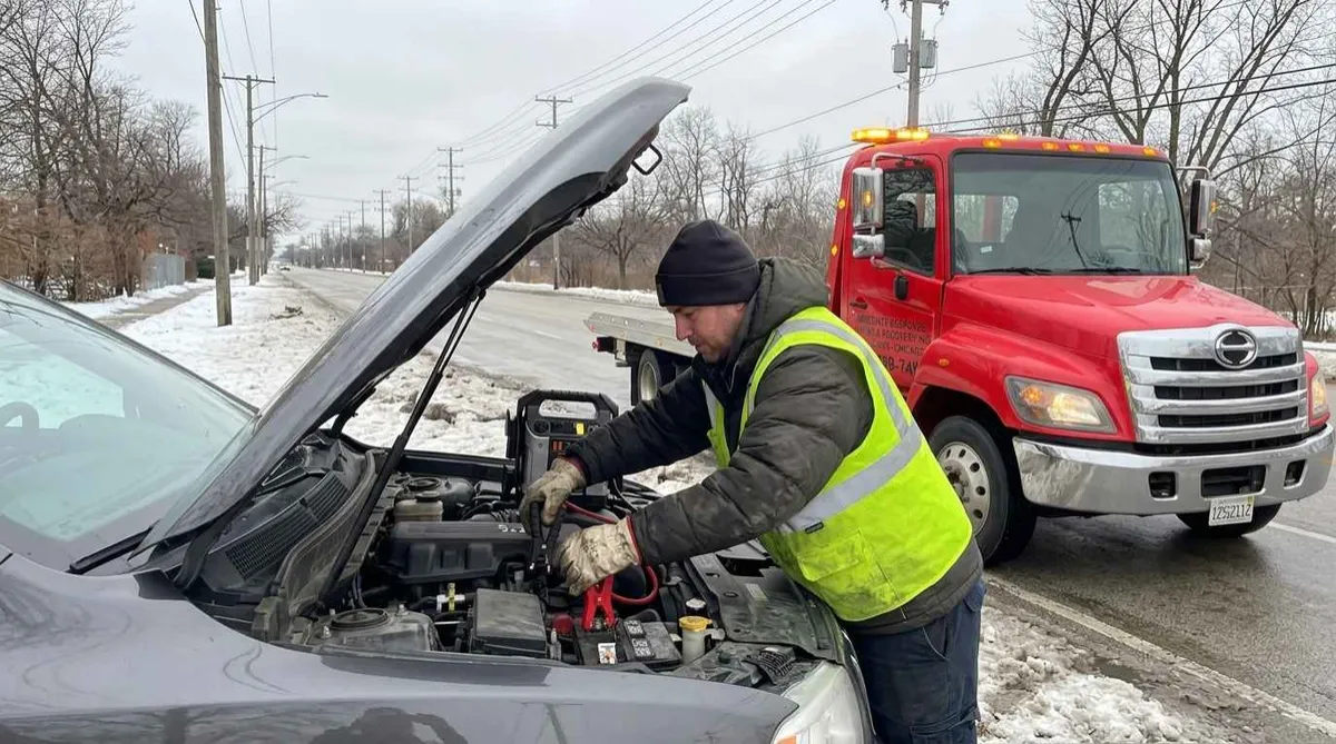 Technician performing battery jump start on SUV in Chicago winter conditions
