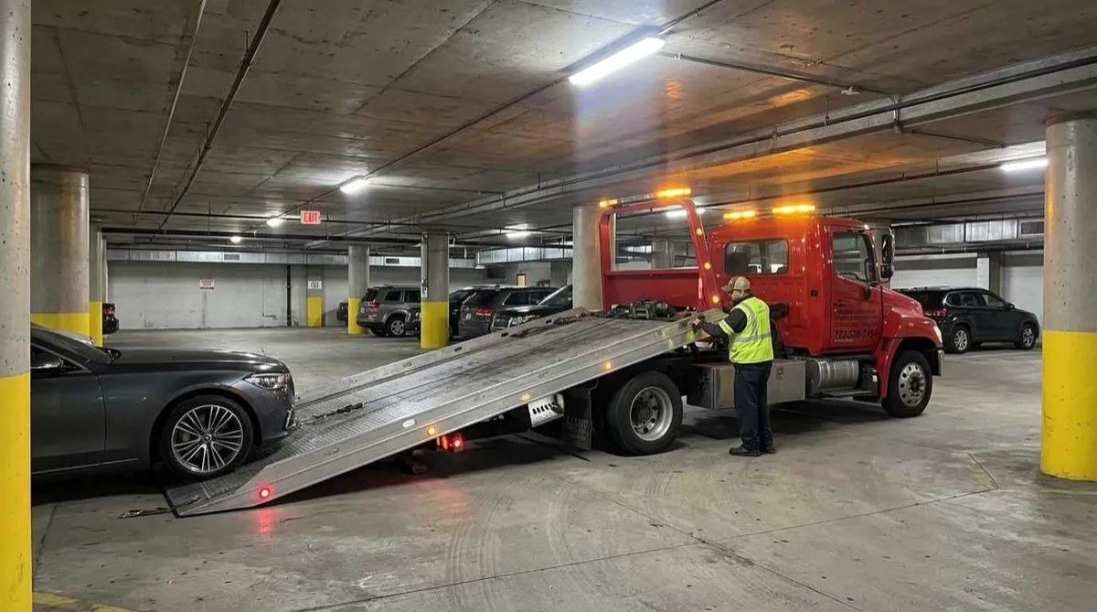 Flatbed tow truck loading a luxury sedan in an underground parking garage, Lincoln Park