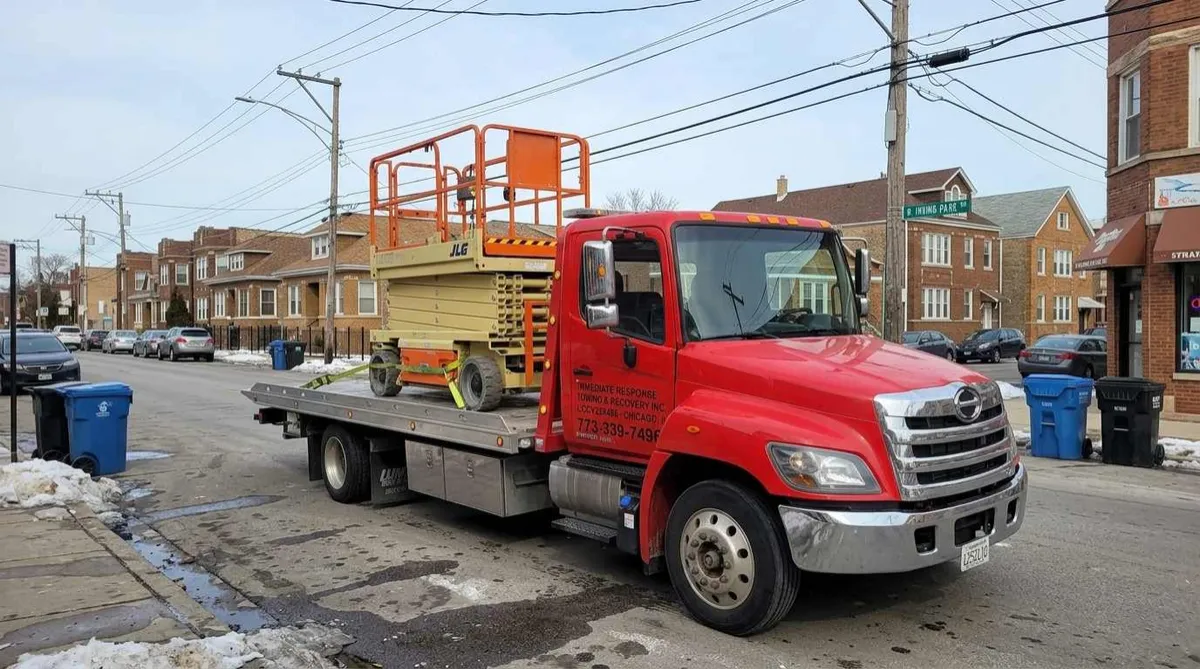 Tow truck transporting a scissor lift for commercial equipment delivery in Dunning, Chicago