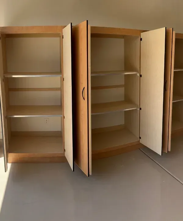 Light wood cabinet doors begin installation in a garage, with one door propped open and a level on top.