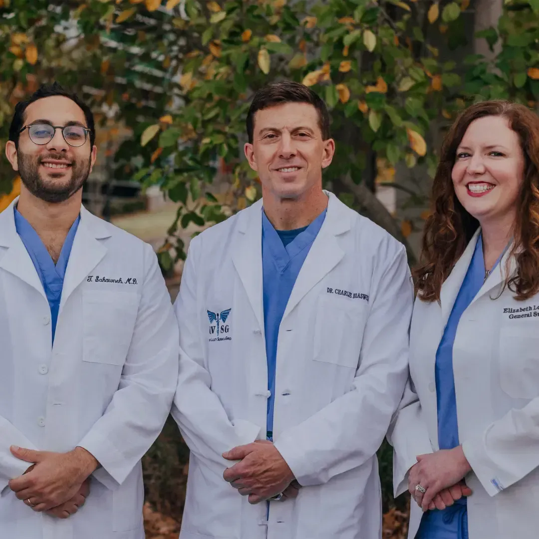 Three medical professionals in white coats standing in front of trees.