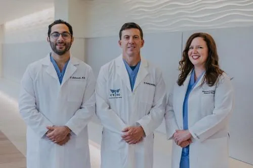 Three medical professionals in white lab coats standing against a wall.