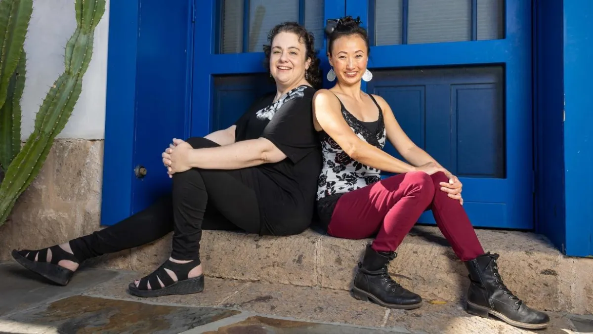 Jennifer Wenzel and Landy Miyake, owners of Root Cause Marketing, sitting in front of a blue door and next to a cactus on a front step in Tucson, AZ