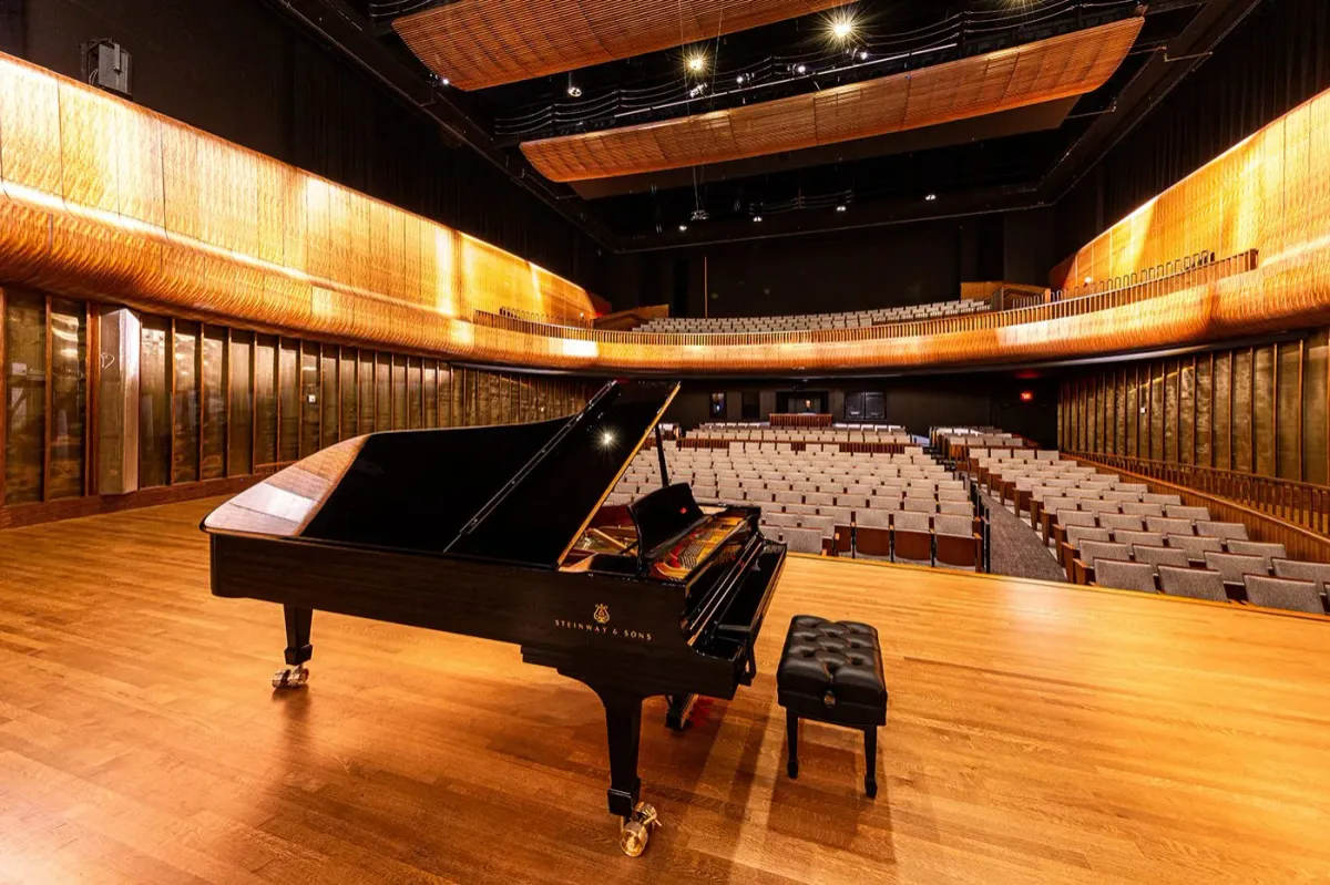The image shows a piano in the middle of a stage amidst a big, empty theater.